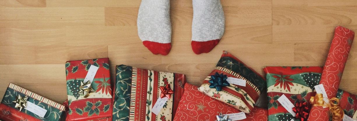 child's feet standing close to Christmas tree where gifts are piled