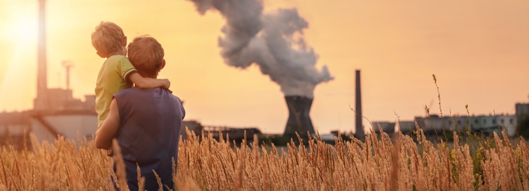man holding child looking across field at polluting smoke stacks