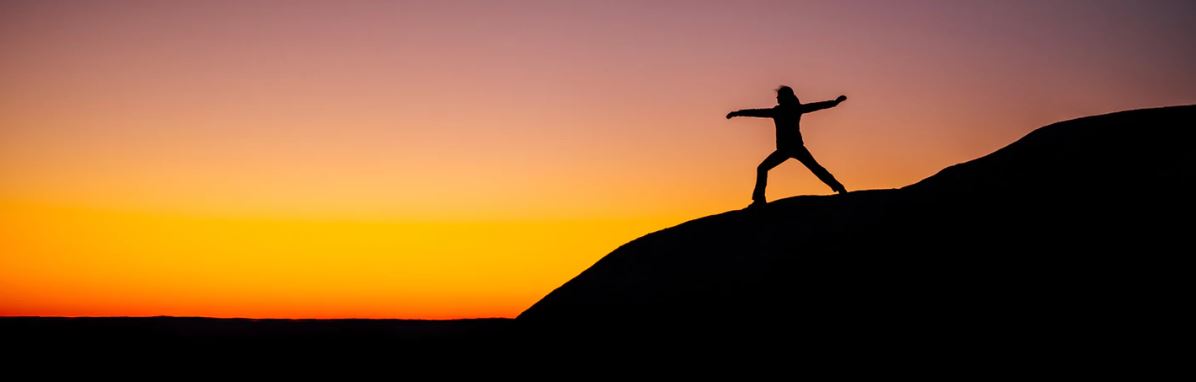 man or woman striking yoga pose on hill top