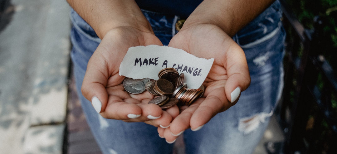 handful of coins with sign that says "make a change"