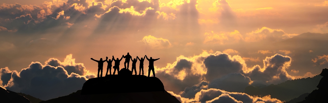 On the top of the world together. A group of people stands on a hill over the beautiful cloudscape.