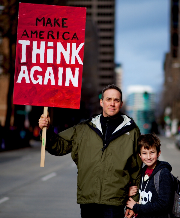 father and son holding sign that reads "make america think again"