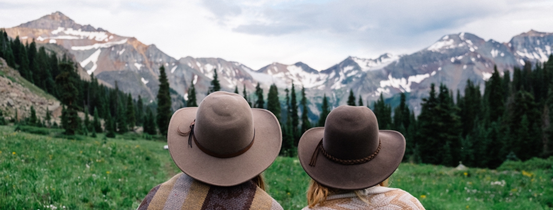 Two women looking across meadow at snow-capped mountains