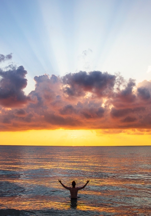 Man standing in ocean looking at sunset