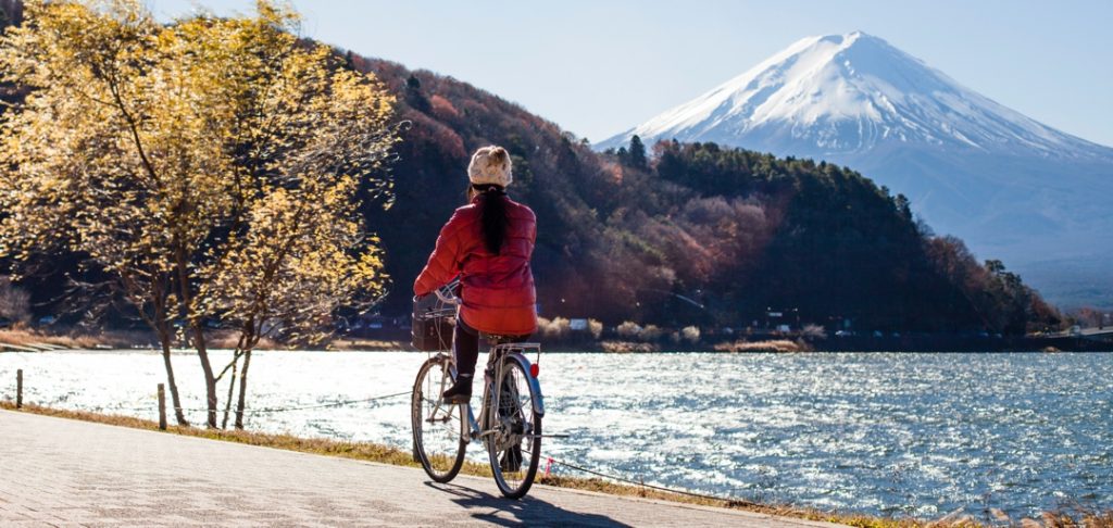 woman riding bicycle beside lake with mountain in the background