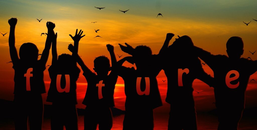 children with arms raised looking facing sunset with the word "future" spelled out across their backs