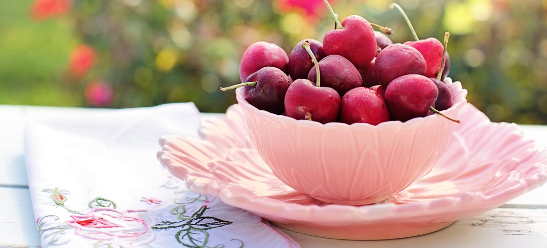 pink bowl full of cherries outdoors with embroidered napkin