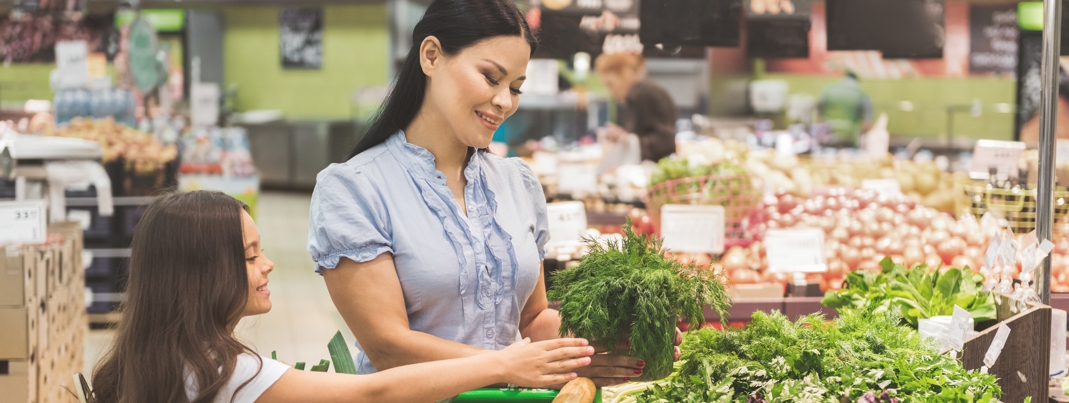 Side view pretty beaming kid and happy mom making choice of fennel in supermarket