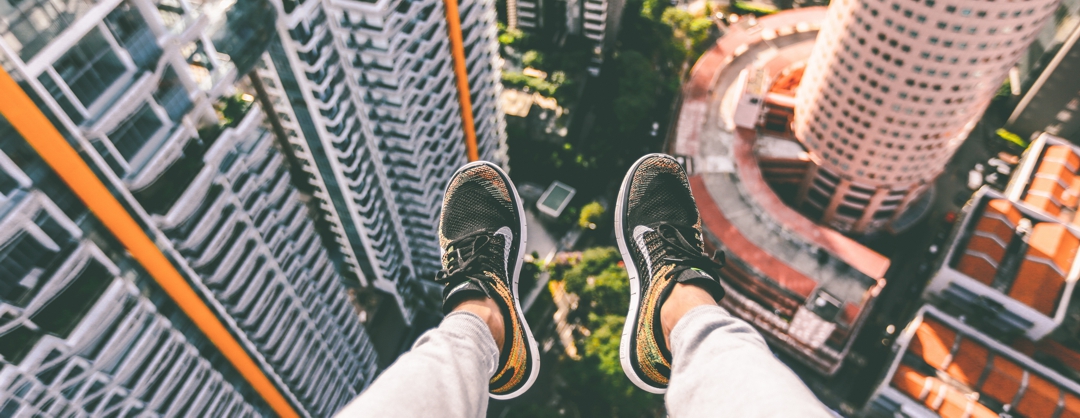 feet with sneakers hanging off the edge of a very tall building