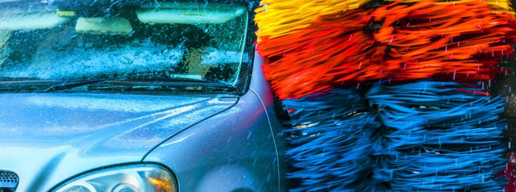 car driving through automated car wash with blue, yellow, and red brushes