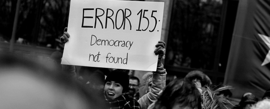 woman at rally holding sign that reads: Error 155: Democracy not found