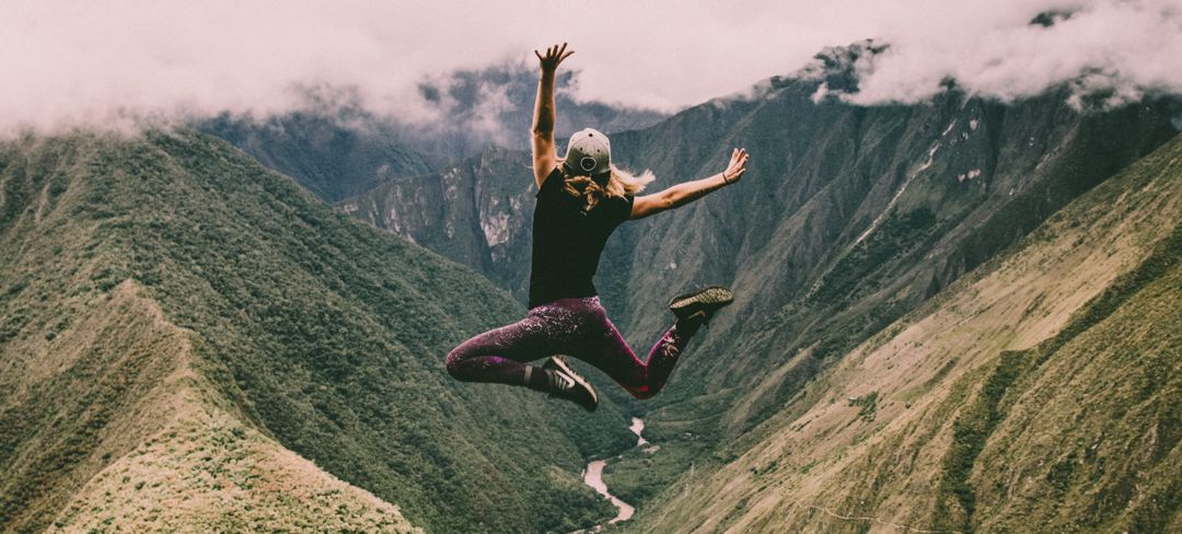 Young woman jumping high in the air with canyon and river in background