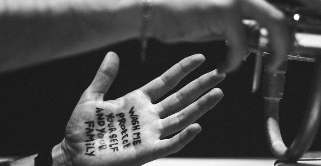 black and white photo of hand with the words "wash me protect yourself and your family" on the palm