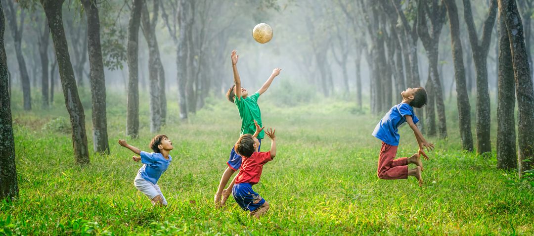 boys playing soccer, jumping for the ball,  in a grassy forest