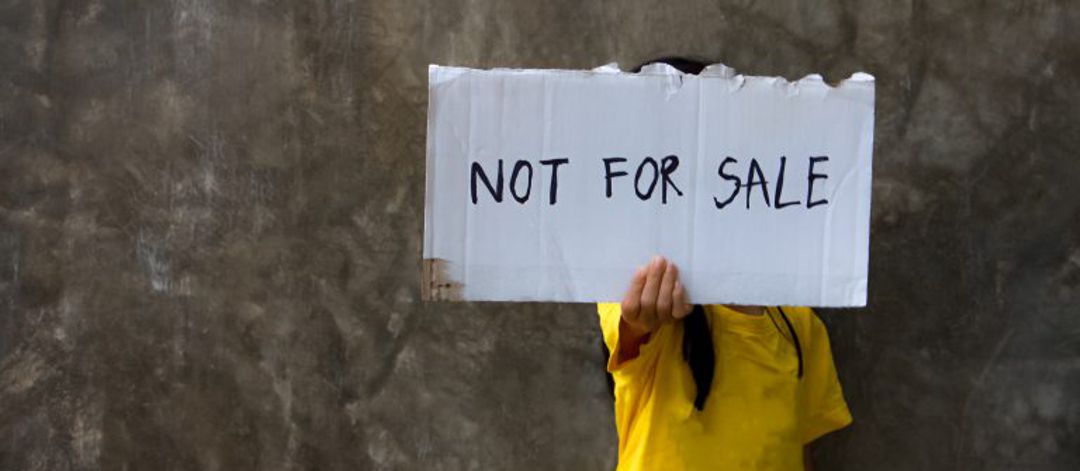 young girl holding sign in front of face that says "not for sale"