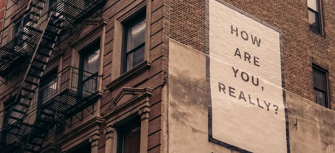 city building with fire escape and sign painted on side that says "how are you doing really?"