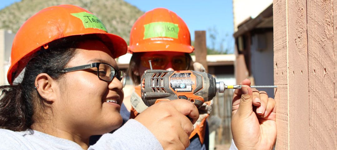 young woman using drill at a home building site with another woman watching