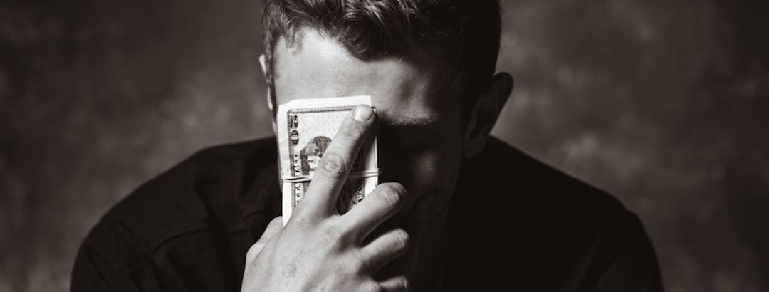 man with head tipped down holding hand to forehead with money in his hand looking worried