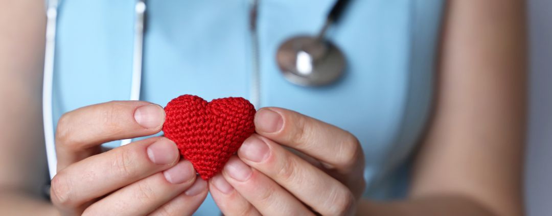 woman nurse or doctor with stethoscope holding red knitted heart in hands