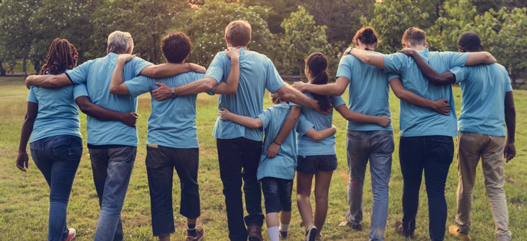 group of volunteers with arms around each other walkiing away from camera toward wooded area