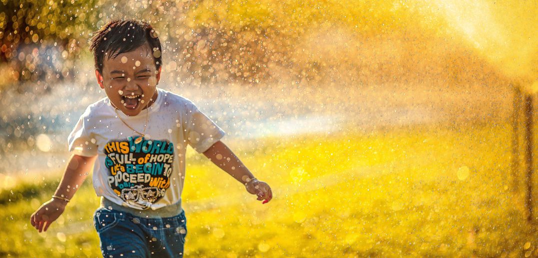 little boy running through sprinkler