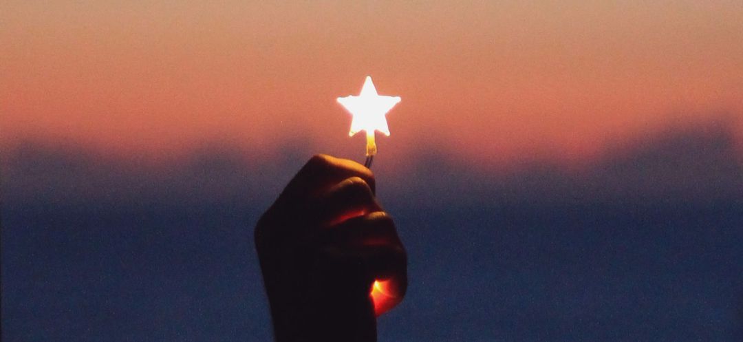 glowing star being held in hand agains a sunset sky