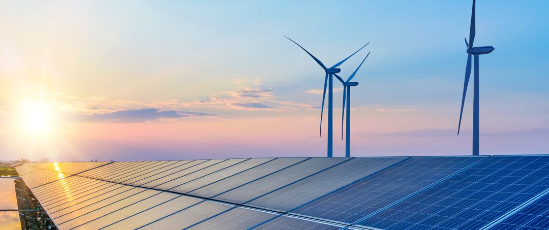 Wind turbines and solar panels against sunset