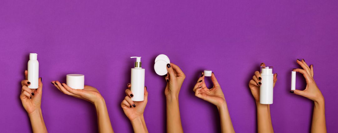 hands holding skin care products on purple background