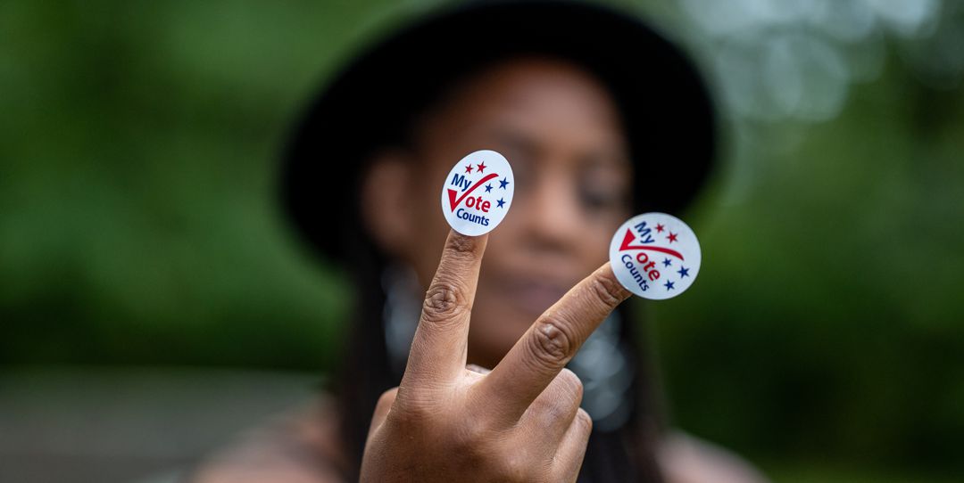 Young black adult wearing stickers on her fingers that say "my vote counts"