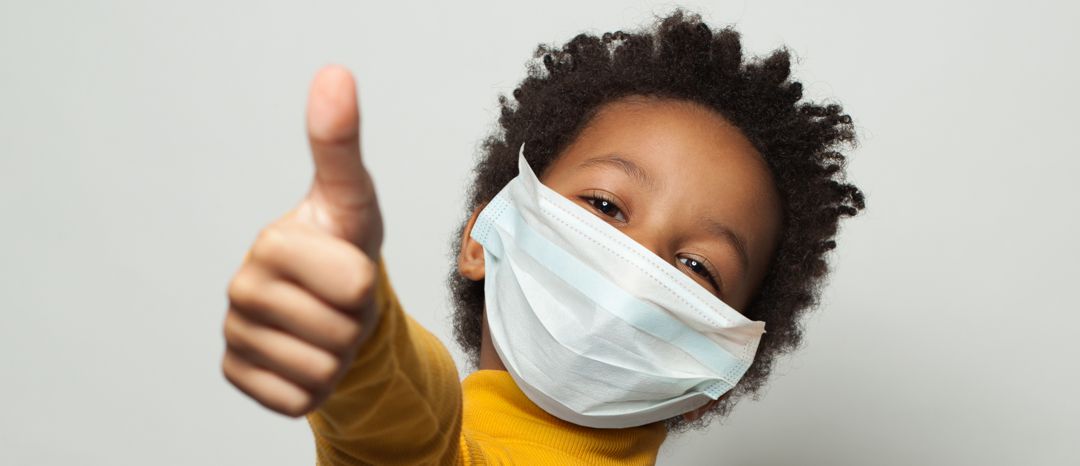 Happy African American black kid in medical protective face mask showing thumb up on white