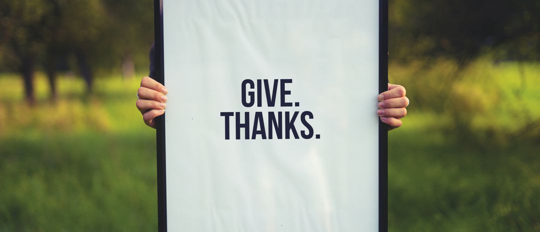 hands holding a sign that says: Give. Thanks.