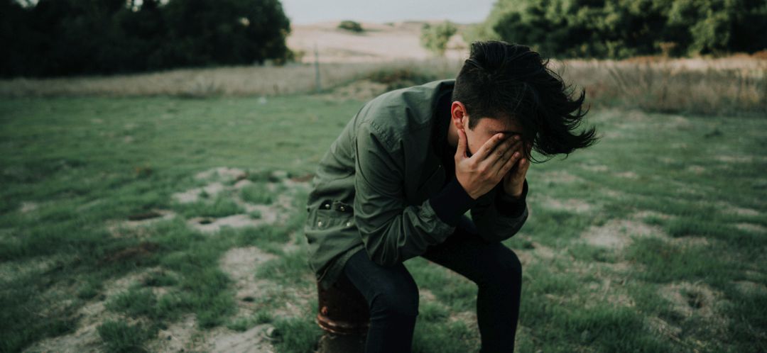 teenage boy sitting in field with face in hands