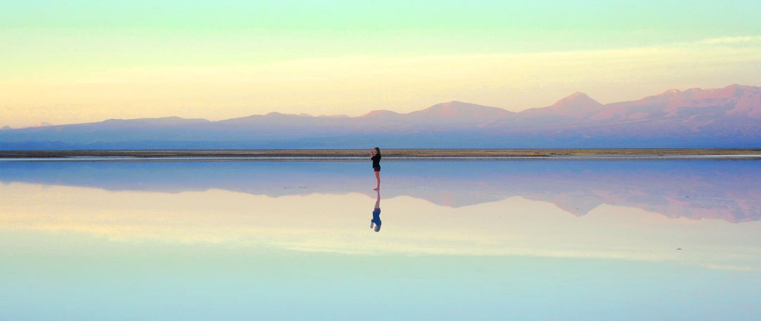 Woman standing alone on a beach with reflection of self in water