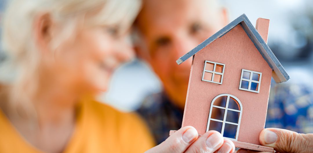 New house concept, happy senior couple holding small home model