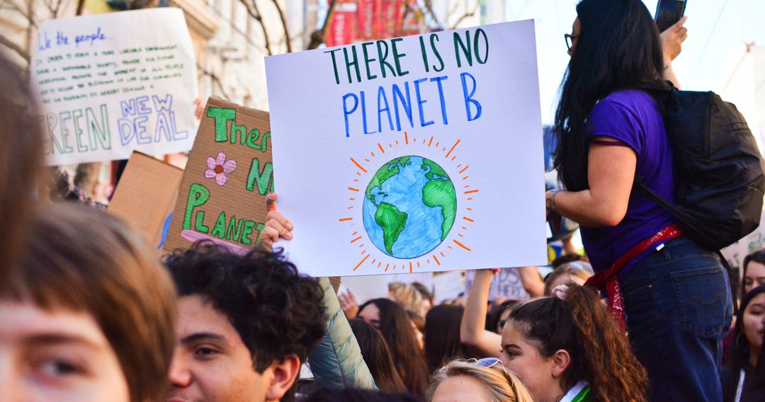 Youth at a rally carring a sign "there is no planet B" girl on platform holding microphone