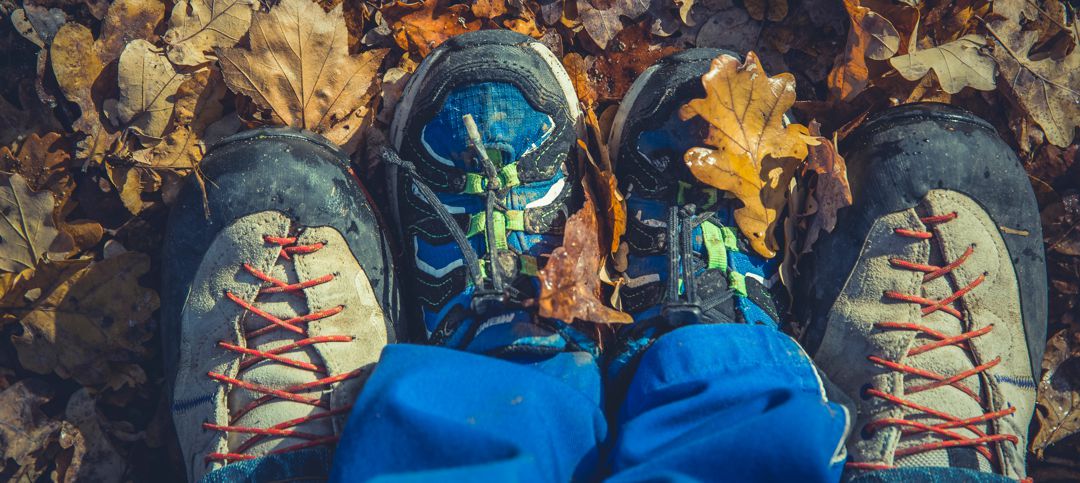 Looking straight down at a pair of men's feet in boots with a child's feet in tennis shoes between adult feet