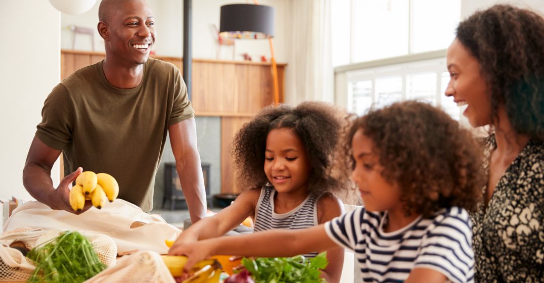 Dad, mom, and two little girls sorting through groceries in cloth shopping bag