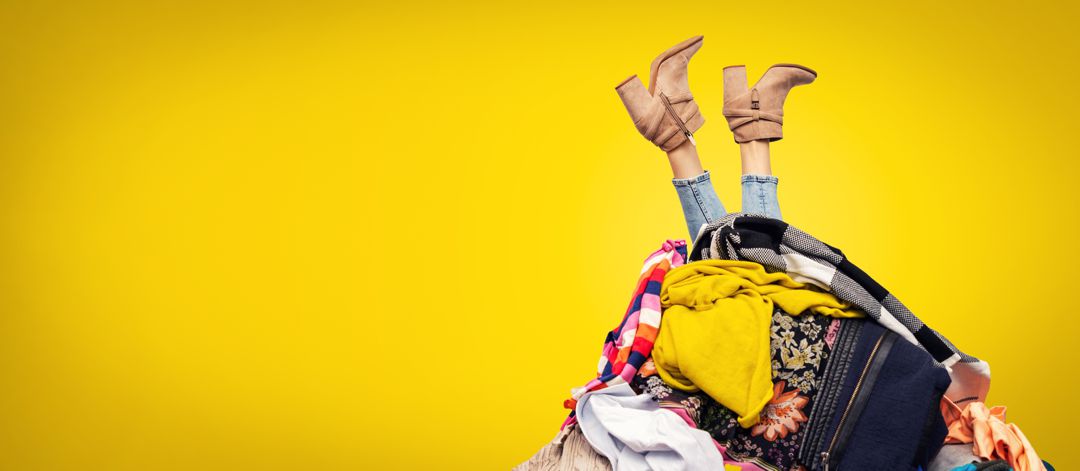 woman's feet wearing boots upsidedown sticking up out of a pile of clothes on yellow background