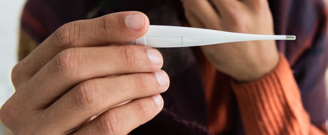 cropped view of sick man with fever holding thermometer in bedroom