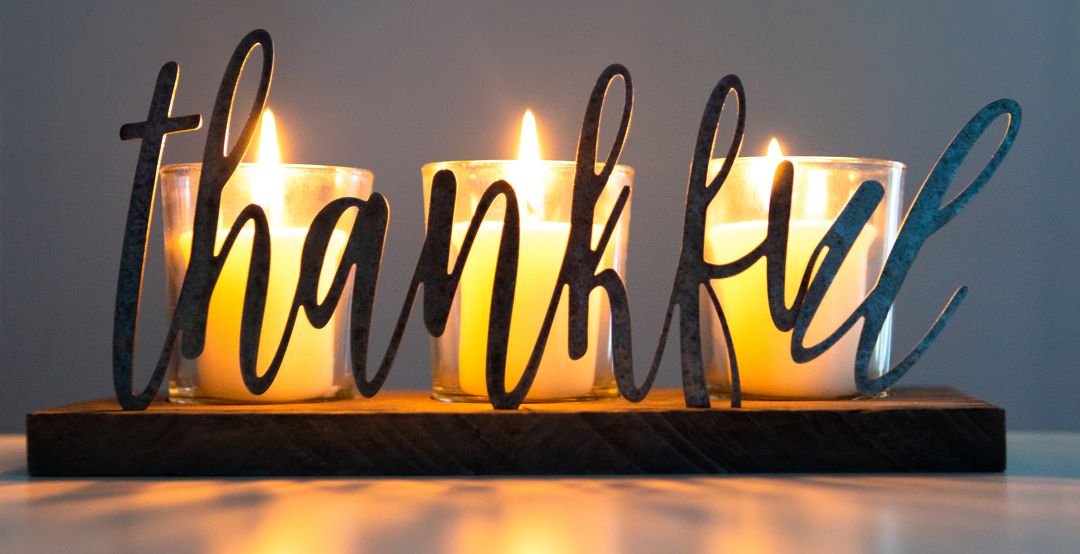 Thankful word candle holder with lit candles illuminating and reflecting on table. Room for text in background.