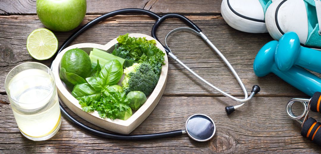 heart shaped bowl full of healthy greens, stethoscope, tennis shoes, and hand weights photographed on barnwood siding
