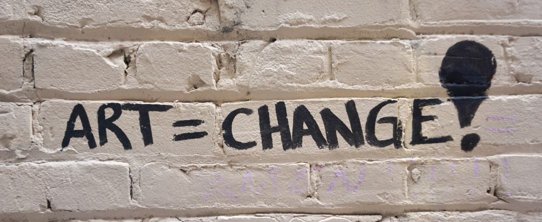 The words art=change! painted on a white brick wall 