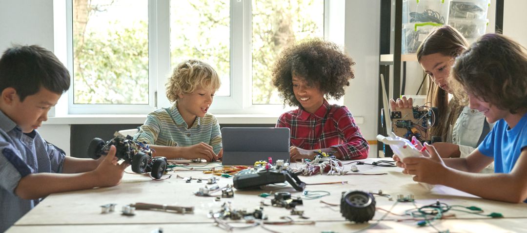 Multiracial school kids students making robotic cars using tablet computer. Diverse junior children pupils building robot vehicle learning at table at STEM code ai engineering science education class.