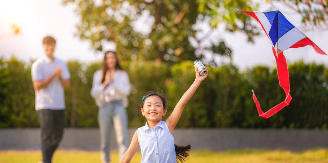 young girl launching kite with parents cheering her on in the background