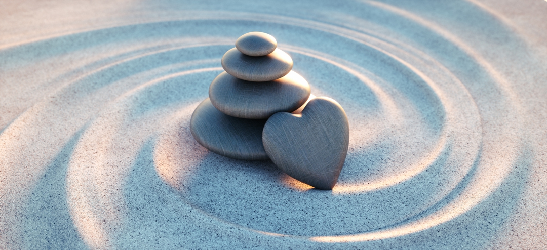 spiral drawn in sand with pile of rocks and heart shaped rock