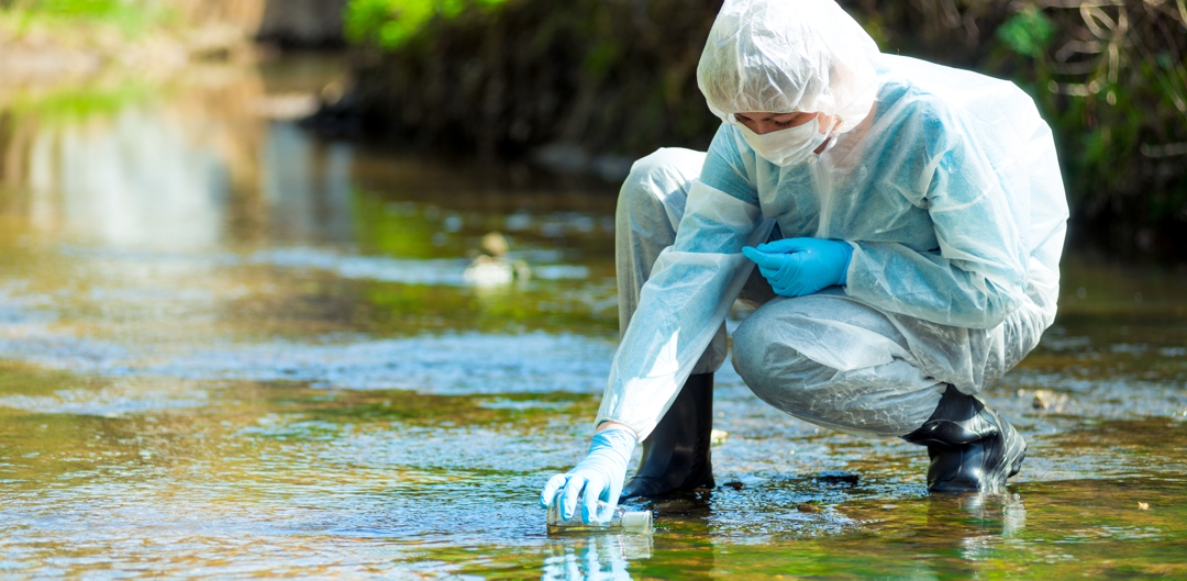 scientist researcher in protective suit takes water for analysis from polluted river