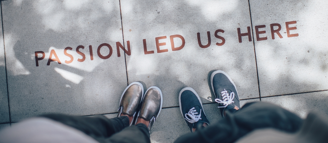 two sets of feet standing on sidewalk where "passion led us here" is written